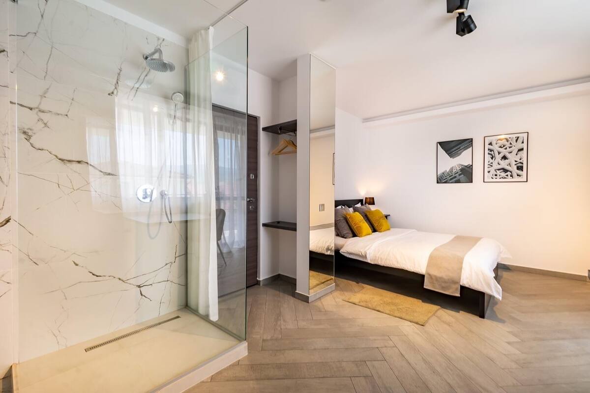 A modern bedroom with a bed, a walk-in closet, and a glass shower enclosure.
