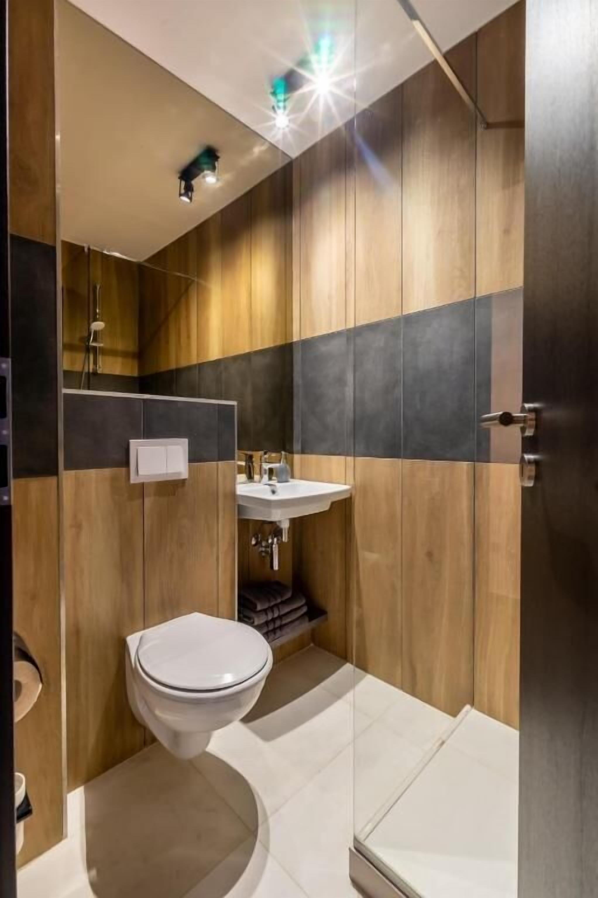 A modern bathroom with a wooden panel design, a white toilet, and a sink with a mirror above it.