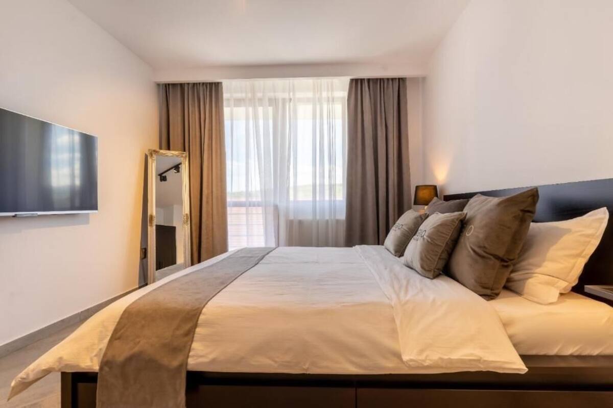 A hotel room with a large bed, a flat-screen TV mounted on the wall, and a window with curtains.