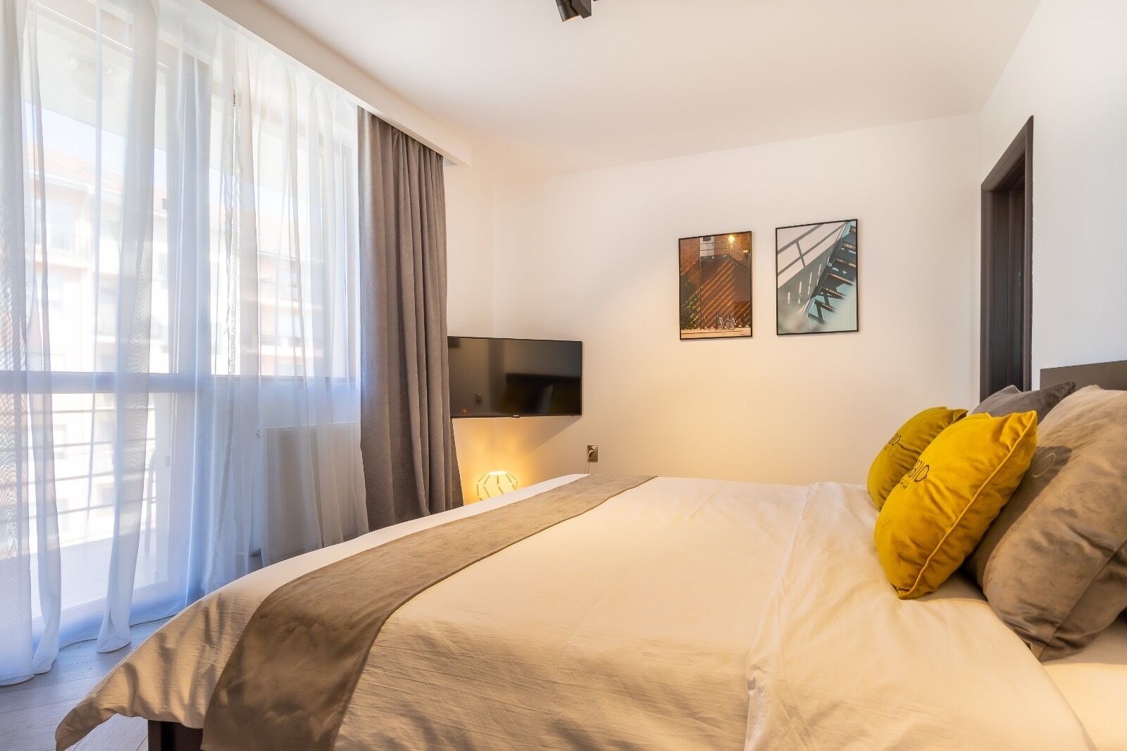 Ein modernes Hotelzimmer mit einem großen Bett, einem an der Wand montierten Fernseher und zwei gerahmten Kunstwerken darüber.