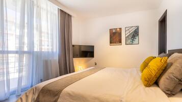 Ein modernes Hotelzimmer mit einem großen Bett, einem an der Wand montierten Fernseher und zwei gerahmten Kunstwerken darüber.