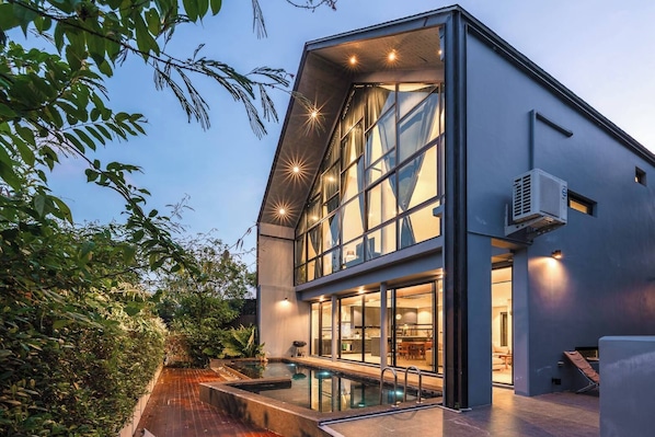 A modern house with a large glass facade, a swimming pool, and a well-lit interior.