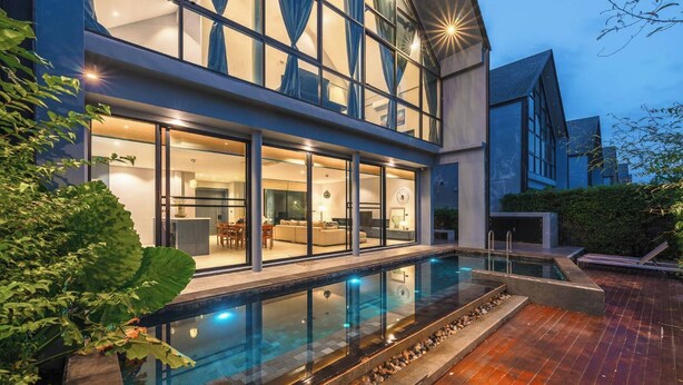 Une maison moderne dotée d’une piscine, de grandes fenêtres et d’un intérieur bien éclairé.