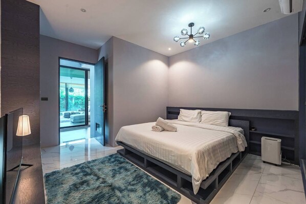 A modern bedroom with a large bed, a ceiling light fixture, and a view of the outdoors.