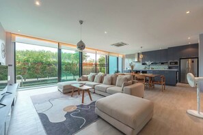 A modern living room with a sofa, a dining table, and a kitchen area with a refrigerator and microwave.