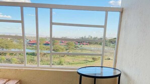 Ein Zimmer mit einem kleinen runden Tisch und einer Bank, ein Fenster mit Blick auf eine Landschaft mit Gebäuden und Grünflächen.