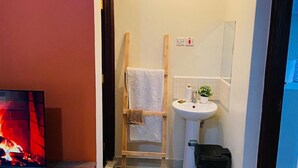 Ein kleines Badezimmer mit Holzstuhl, Waschbecken, Spiegel und Fernseher, der einen Kamin zeigt.
