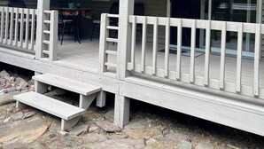 A covered porch with a wooden deck, stone steps, and a railing. - Private 27 acres in peaceful Tapiola MI   Great home base to explore Western UP. (Chassell)