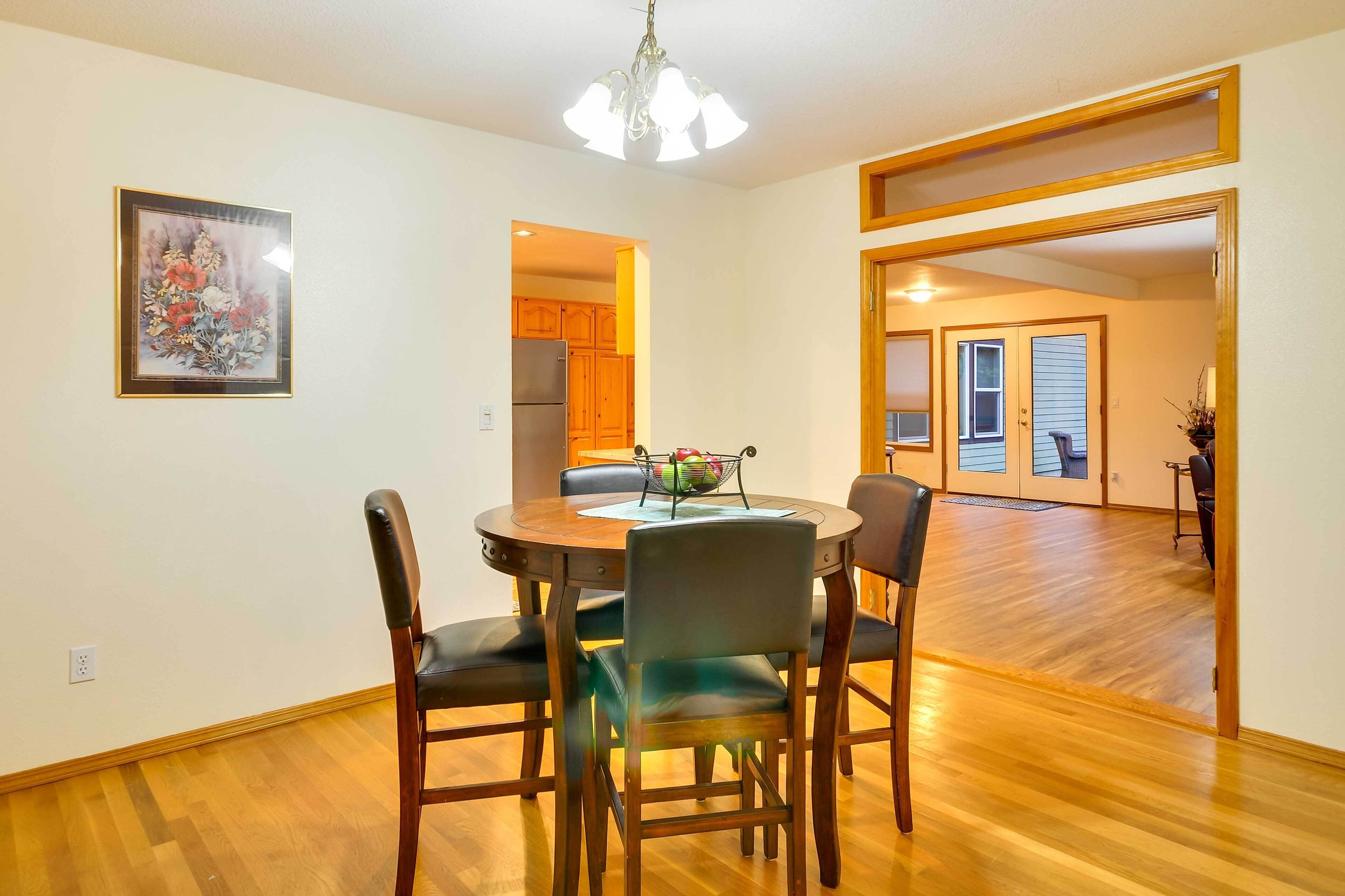 A dining area with a round table, four chairs, a chandelier, and a framed picture on the wall.