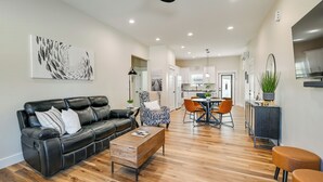 A modern living room with a black leather sofa, a wooden coffee table, and a dining area with orange chairs. - Near CU & Dtwn! Campbellsville Home w/ Game Room (Campbellsville)