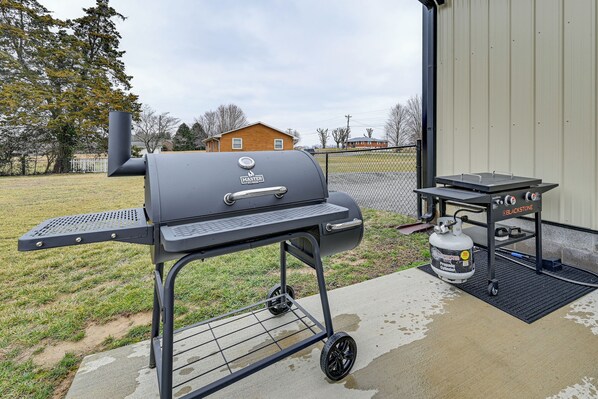 A portable grill with a side table and a propane tank on a concrete patio.