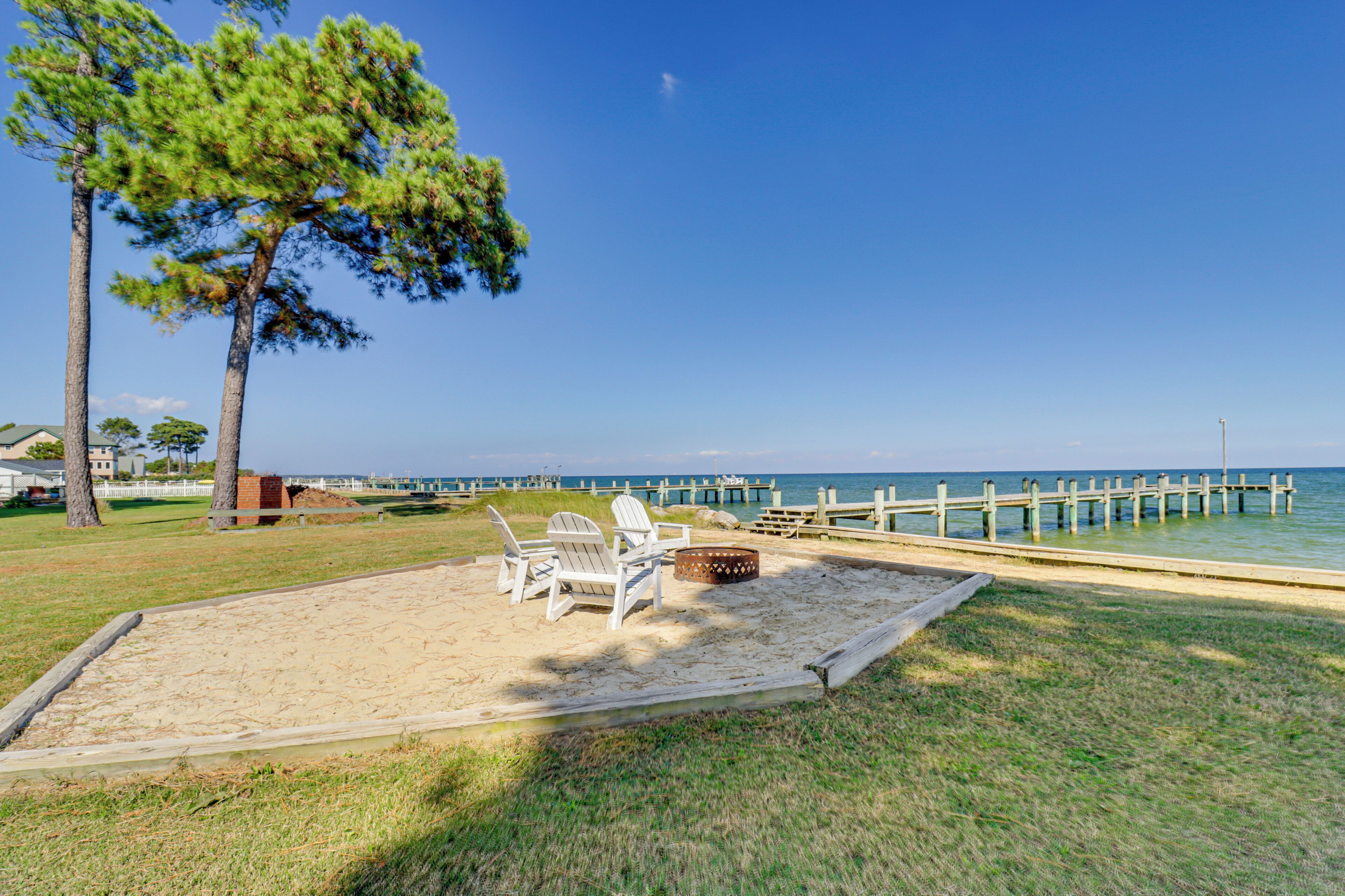 A beach area with a wooden deck, beach chairs, and a fire pit.
