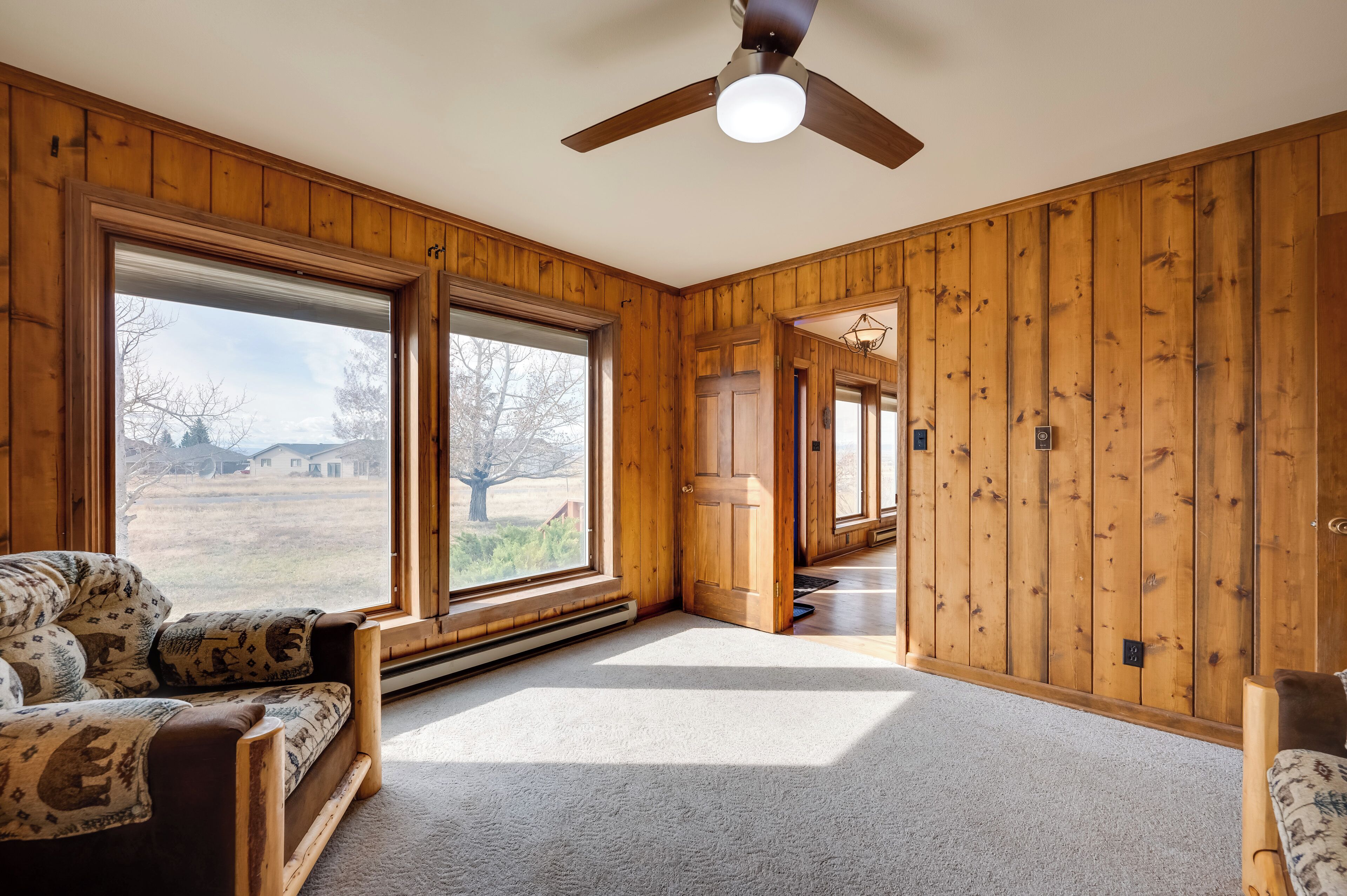 A room with wooden walls, a ceiling fan, and large windows offering a view of the outdoors.