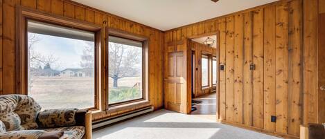 A room with wooden walls, a ceiling fan, and large windows offering a view of the outdoors.