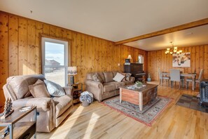 A cozy living room with wooden walls, a leather sofa, a coffee table, and a dining area with a chandelier. - Charming Country Home in Laramie - 4 Mi to UW! (Laramie)