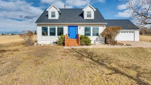 A two-story house with a blue front door, a garage, and a small porch with steps. - Charming Country Home in Laramie - 4 Mi to UW! (Laramie)