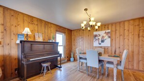 A wooden-paneled room with a piano, dining table, chairs, and a chandelier. - Charming Country Home in Laramie - 4 Mi to UW! (Laramie)