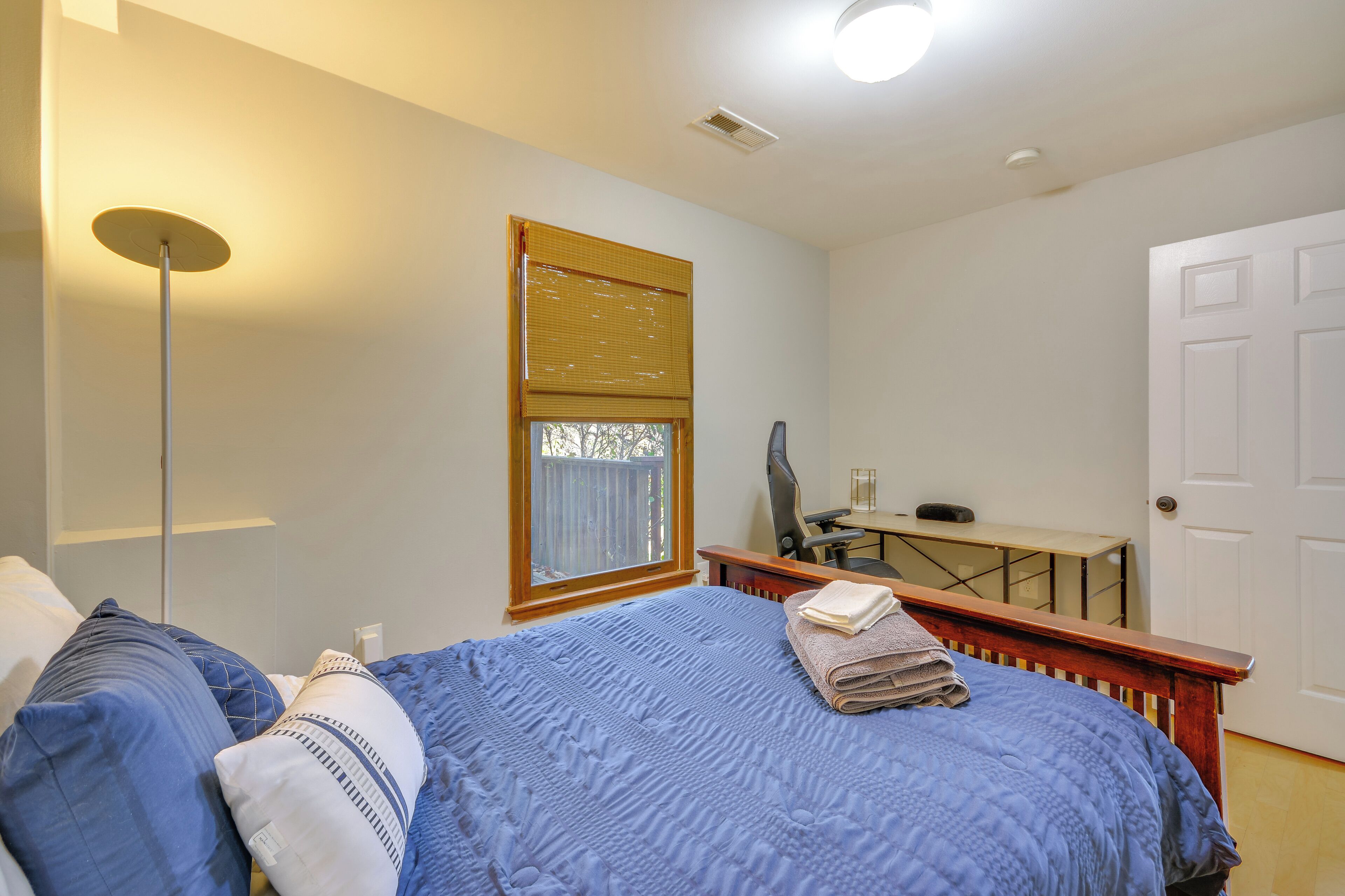 Une chambre à coucher avec un lit, un bureau, une chaise et une fenêtre avec des stores.