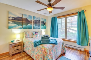 Une chambre à coucher avec un lit, une table de chevet, un ventilateur de plafond et une fenêtre avec des rideaux.