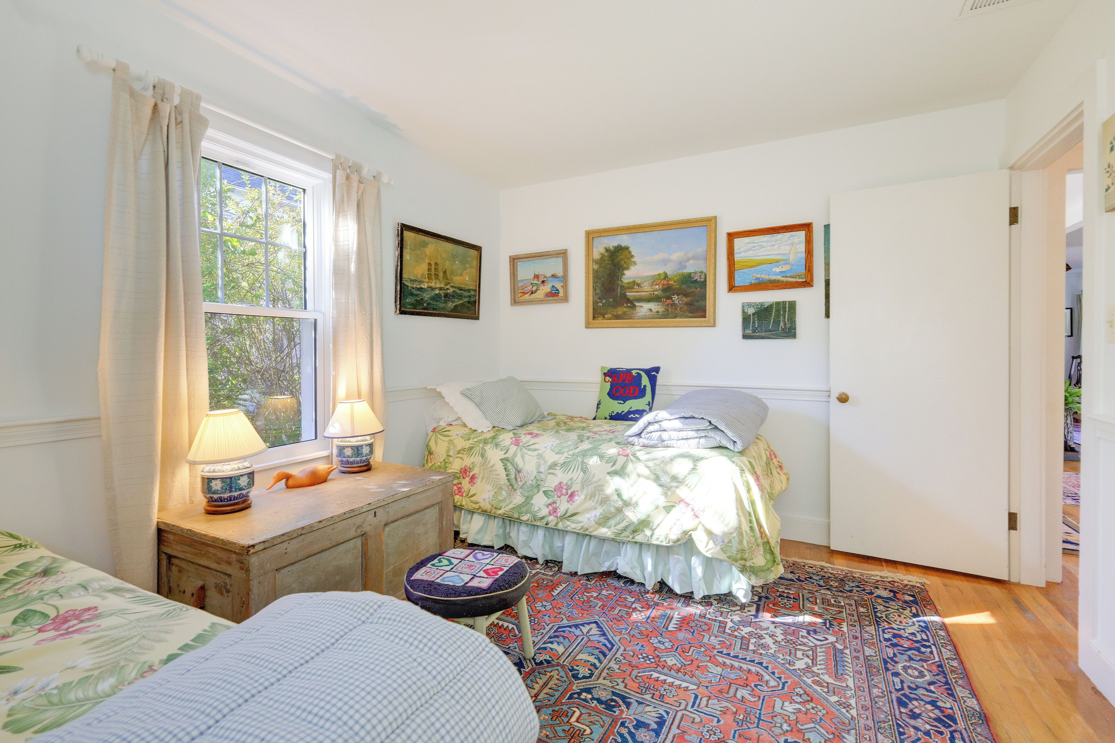 Quarto com cama, mesa de cabeceira, luminária, janela com cortinas e tapete.