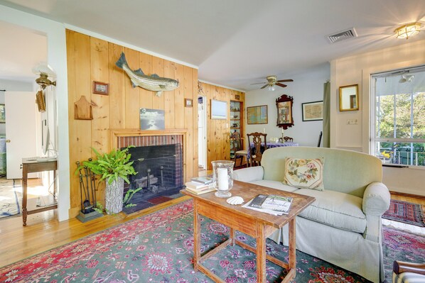 A cozy living room with a fireplace, wooden walls, a green sofa, and a patterned rug. - Walk to Beach & Main St Hyannis: Cape Cod Home! (Hyannis)