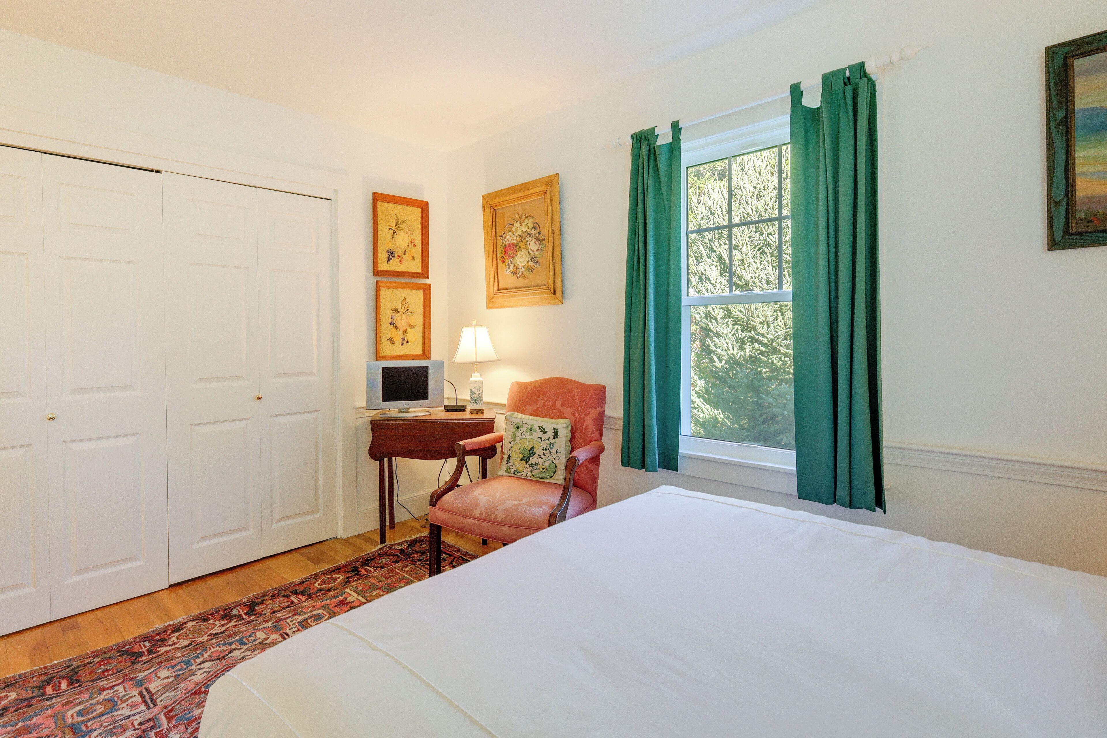 Une chambre à coucher avec un lit, un bureau avec une lampe, une chaise et une fenêtre avec des rideaux.