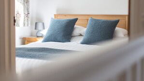Ein ordentlich gemachtes Bett mit blauen Kissen und einer weißen Decke in einem Zimmer mit einem hölzernen Kopfschild.