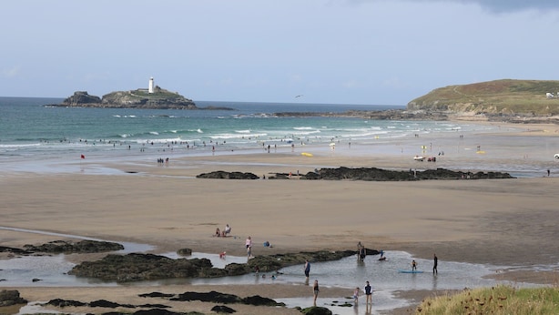 Ein Strand mit einem Leuchtturm, Felsen und Menschen, die das Wasser genießen.