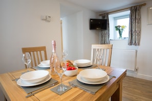 A dining table set with plates, glasses, and a bottle, with a window and curtains in the background.