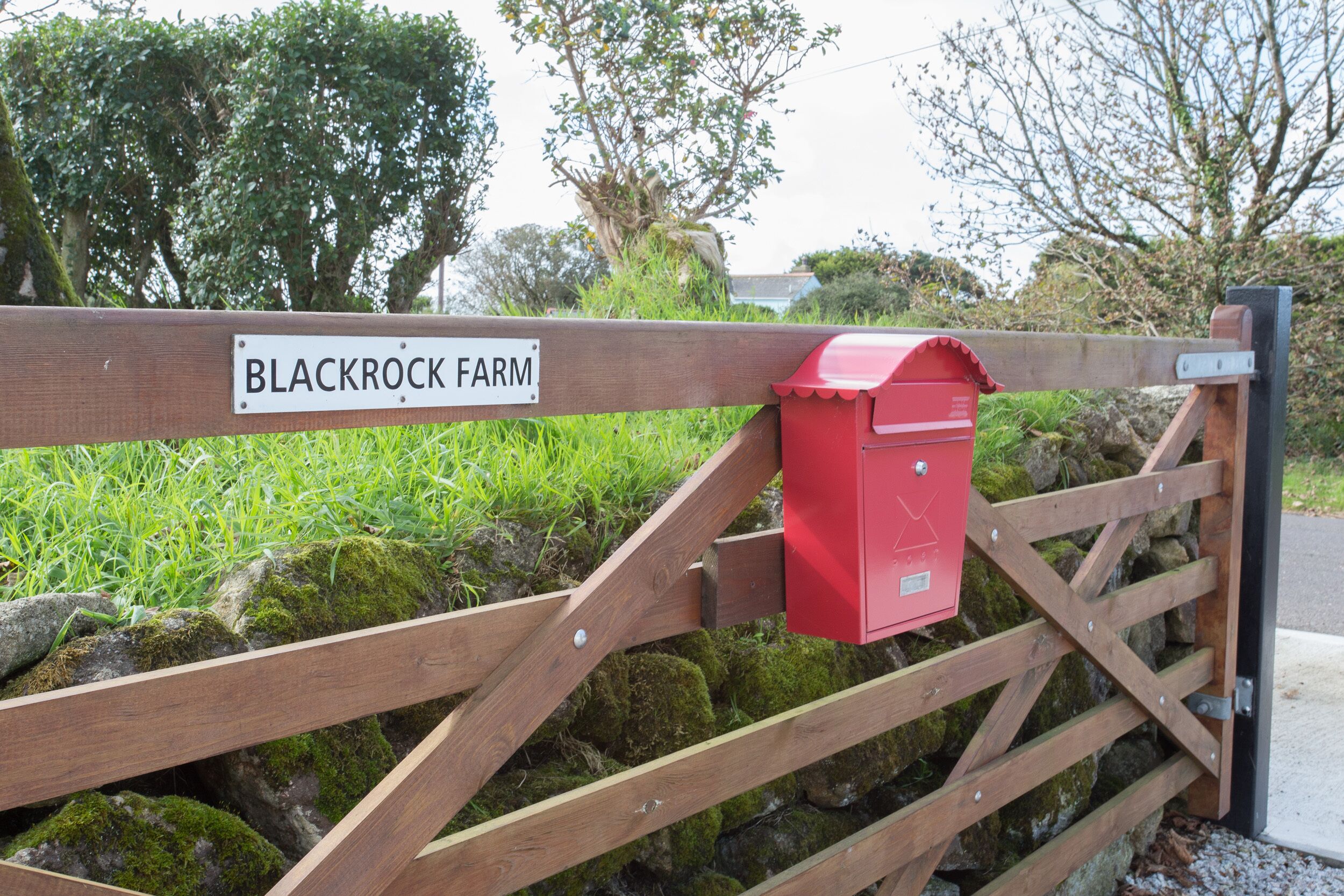 A wooden gate with a sign reading "BLACKROCK FARM" and a red mailbox attached to it.