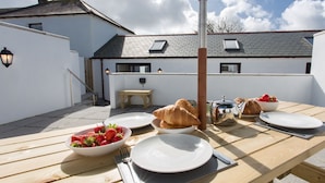 Ein Holztisch ist für das Frühstück gedeckt, mit Tellern, Croissants und einer Schale Erdbeeren.