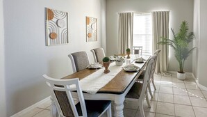 Ein Esszimmer mit einem rechteckigen Tisch, weißen Stühlen und zwei an der Wand befestigten abstrakten Kunstwerken.