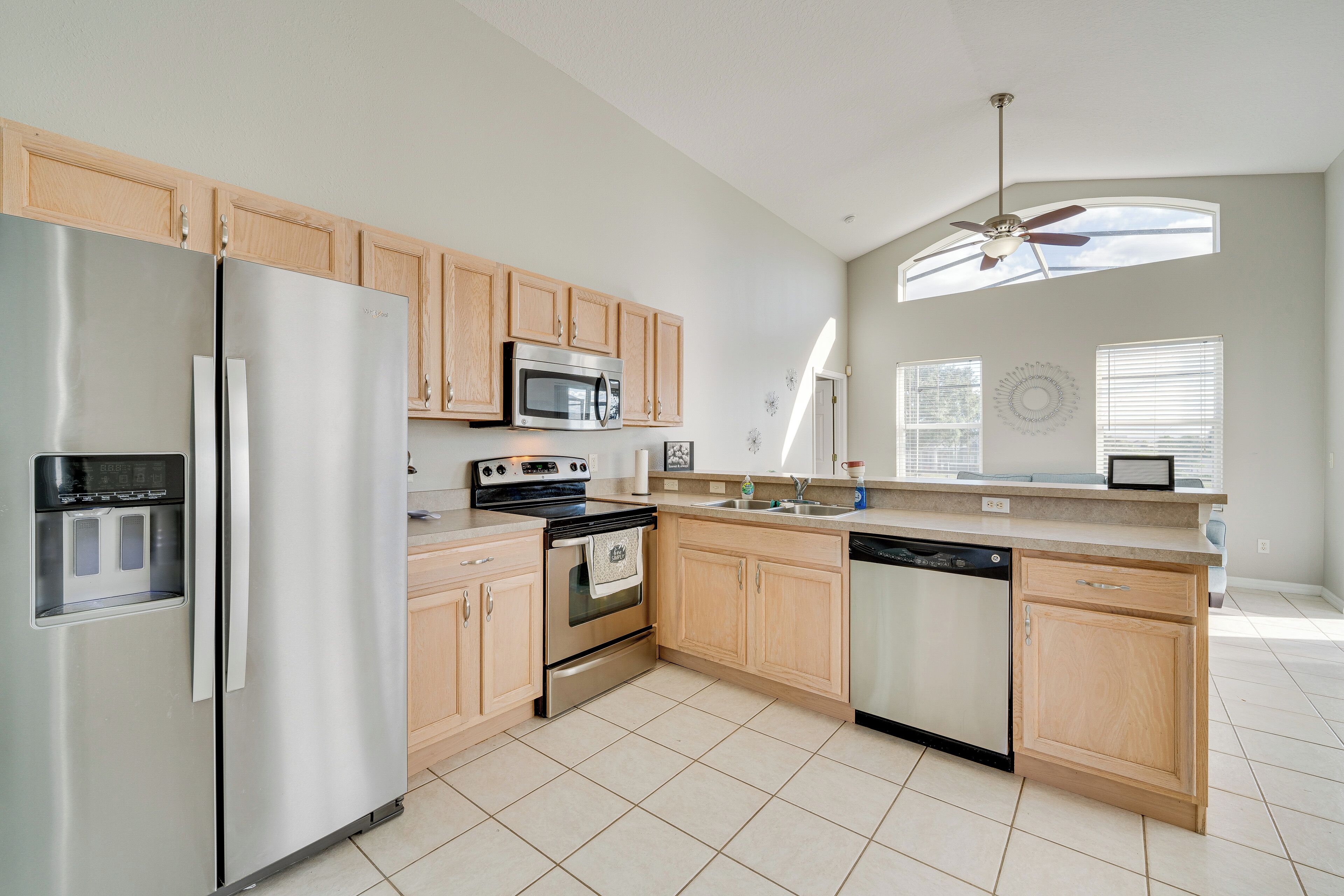 A modern kitchen with stainless steel appliances, wooden cabinets, and a large window providing natural light.