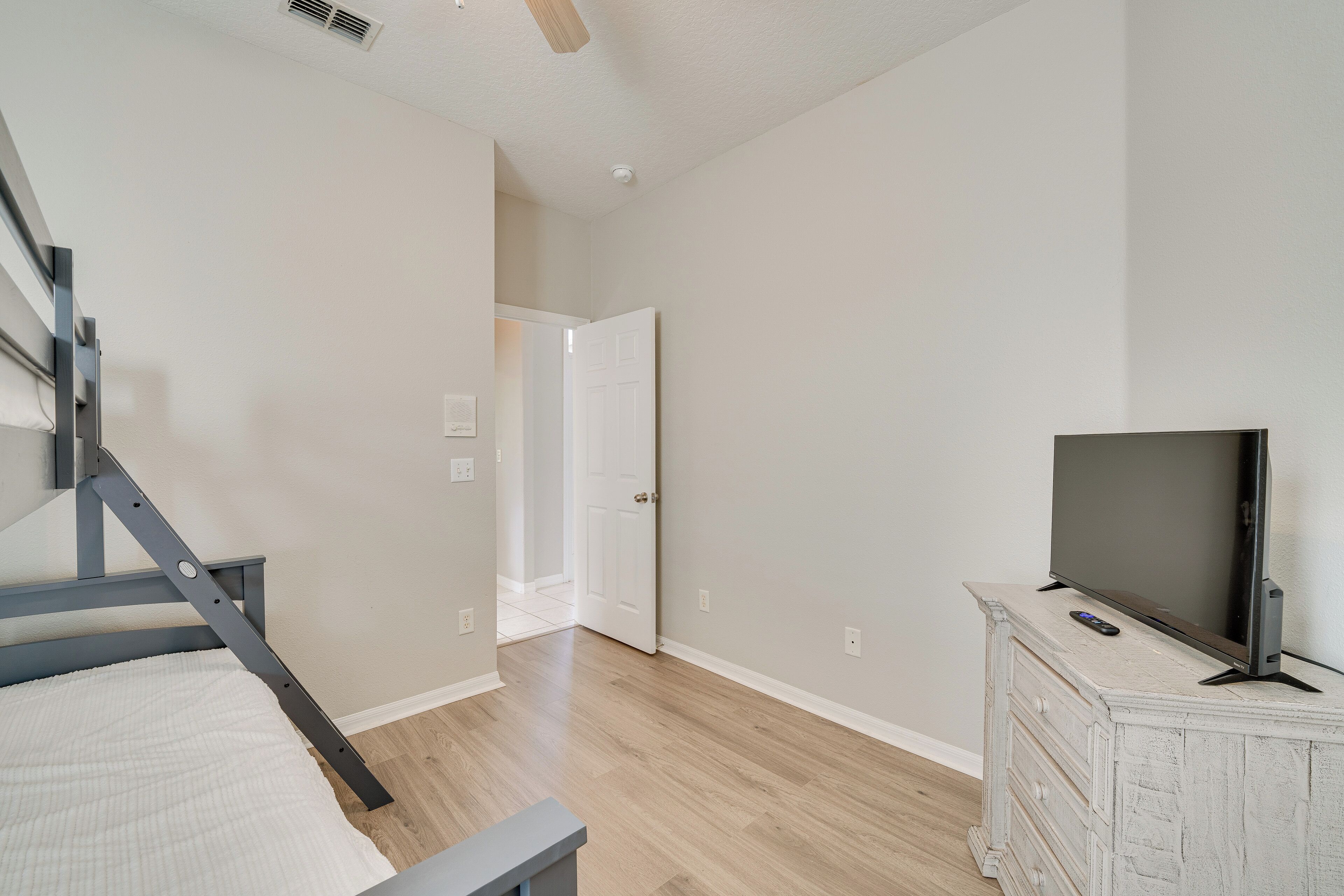 A bedroom with a bed, a dresser, a television, and a door leading to another room.