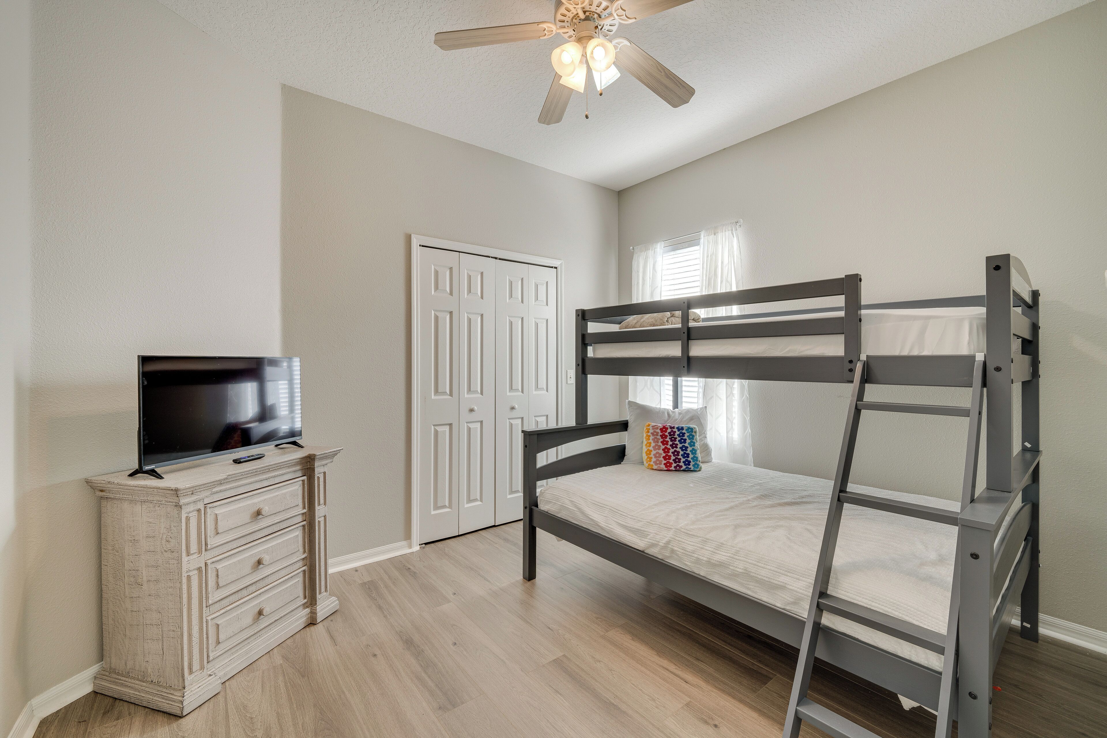 Une chambre avec un lit superposé, une commode, un téléviseur et un ventilateur de plafond.