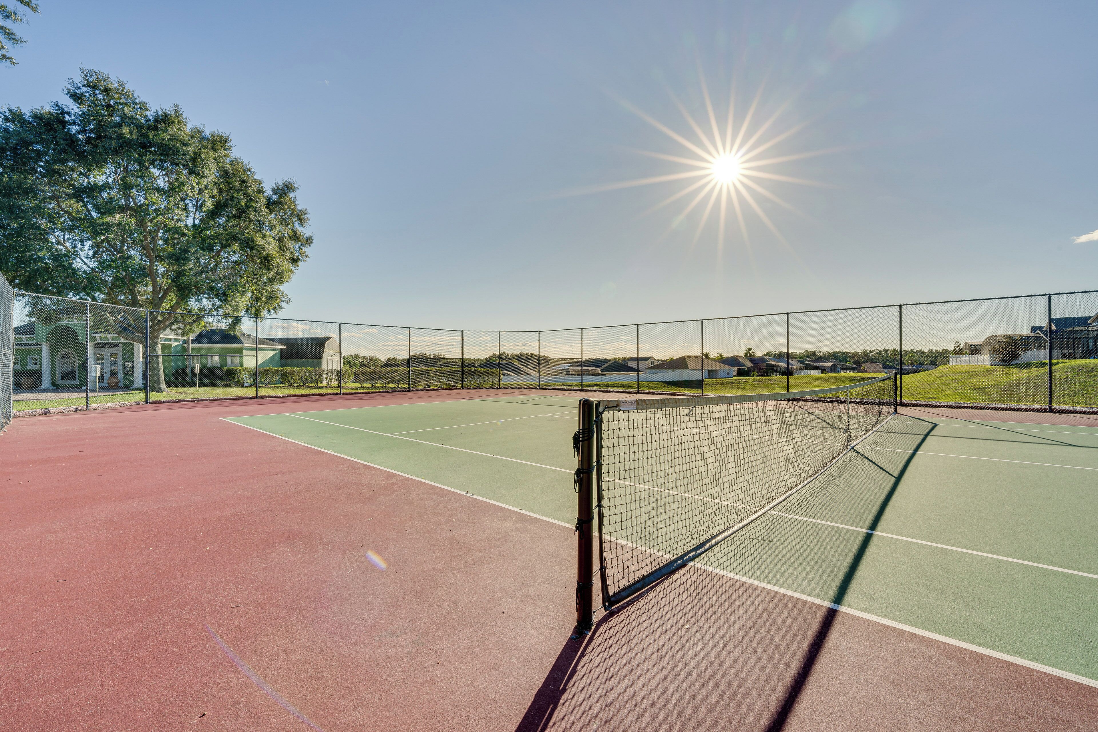 Un court de tennis avec un filet, entouré d’une clôture et d’arbres.