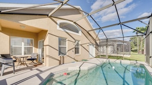 Ein Schwimmbecken mit Glasveranda, eine Terrasse mit Stühlen und Tisch sowie der Blick auf eine Wohngegend.