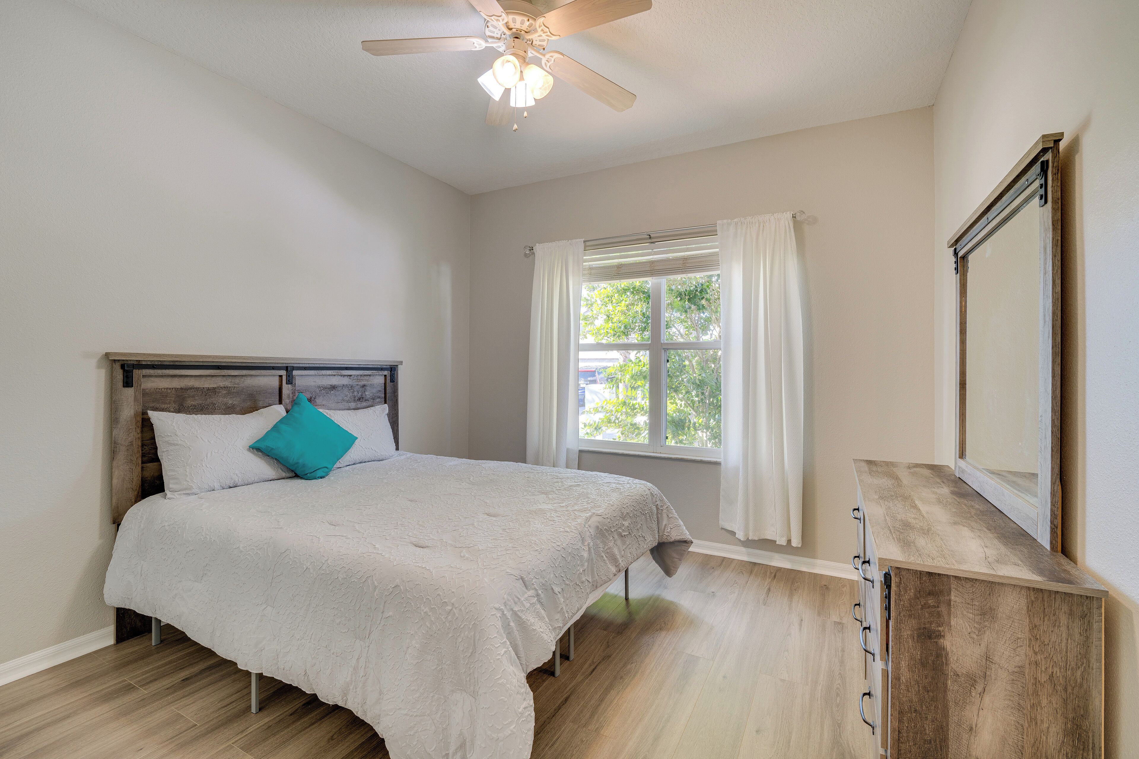 A bedroom with a bed, a ceiling fan, a window with curtains, and a dresser.