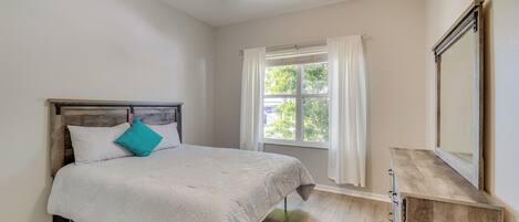 A bedroom with a bed, a ceiling fan, a window with curtains, and a dresser.
