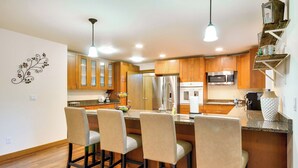 A modern kitchen with wooden cabinets, a stainless steel refrigerator, a microwave, and a bar area with four stools. - Dog-friendly Milwaukie Home: 9 Mi to Dtwn Portland (Milwaukie)