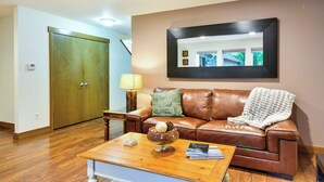 A living room with a brown leather sofa, a wooden coffee table, and a large mirror on the wall. - Dog-friendly Milwaukie Home: 9 Mi to Dtwn Portland (Milwaukie)