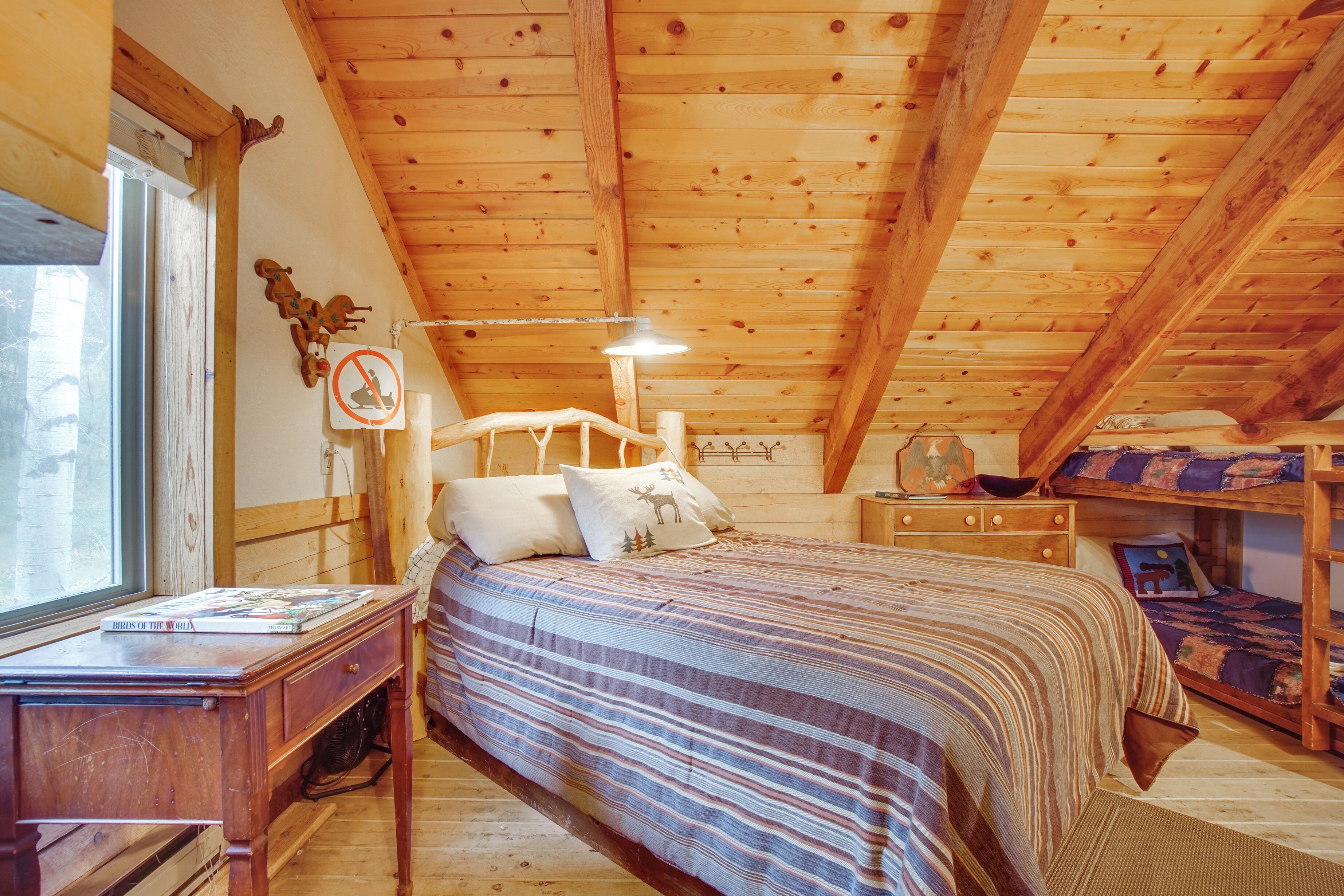 A wooden cabin bedroom with a bunk bed, a desk with a book, a window, and a no-smoking sign.