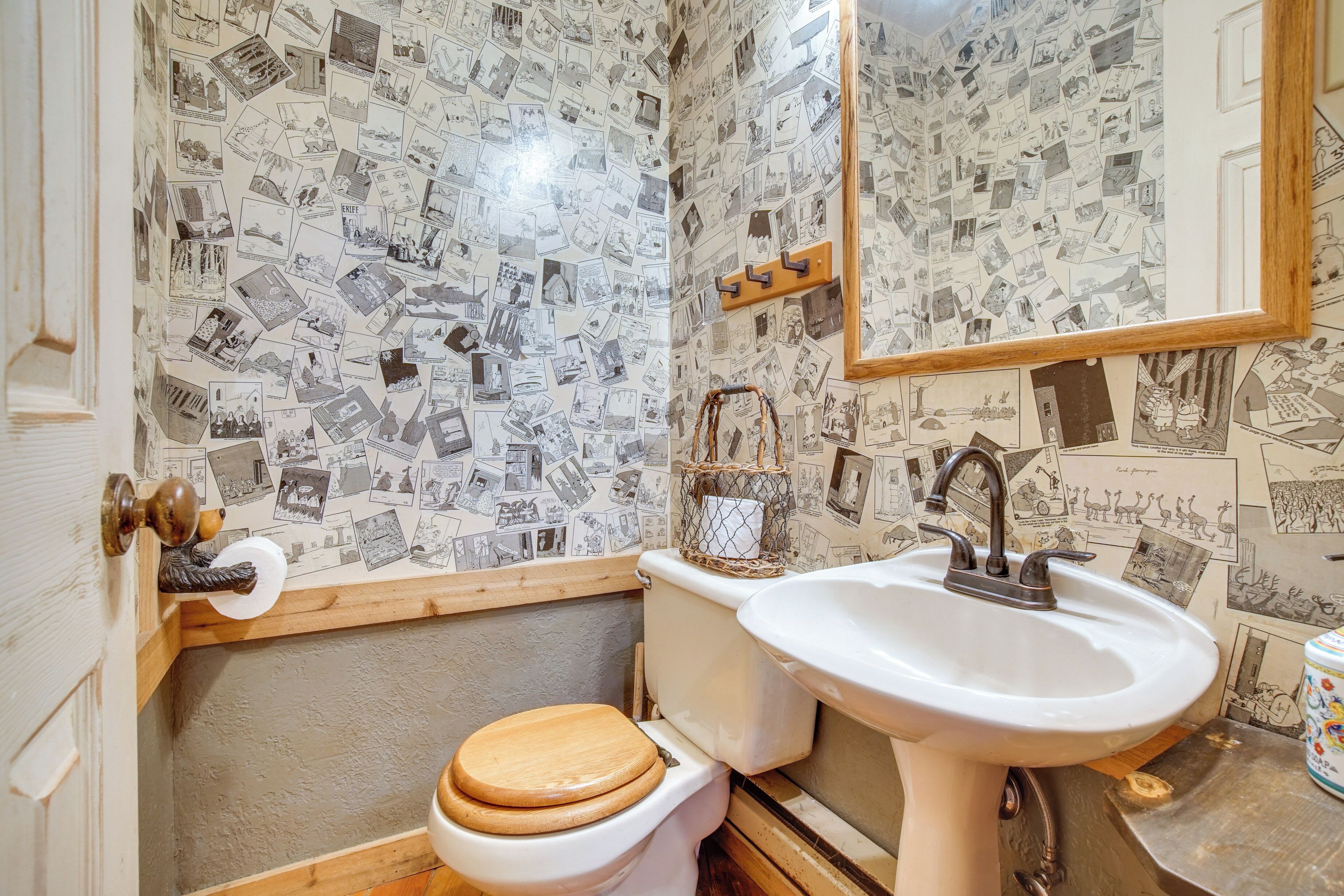 A bathroom with a toilet, sink, and mirror. The walls are covered with a pattern of black and white photographs.