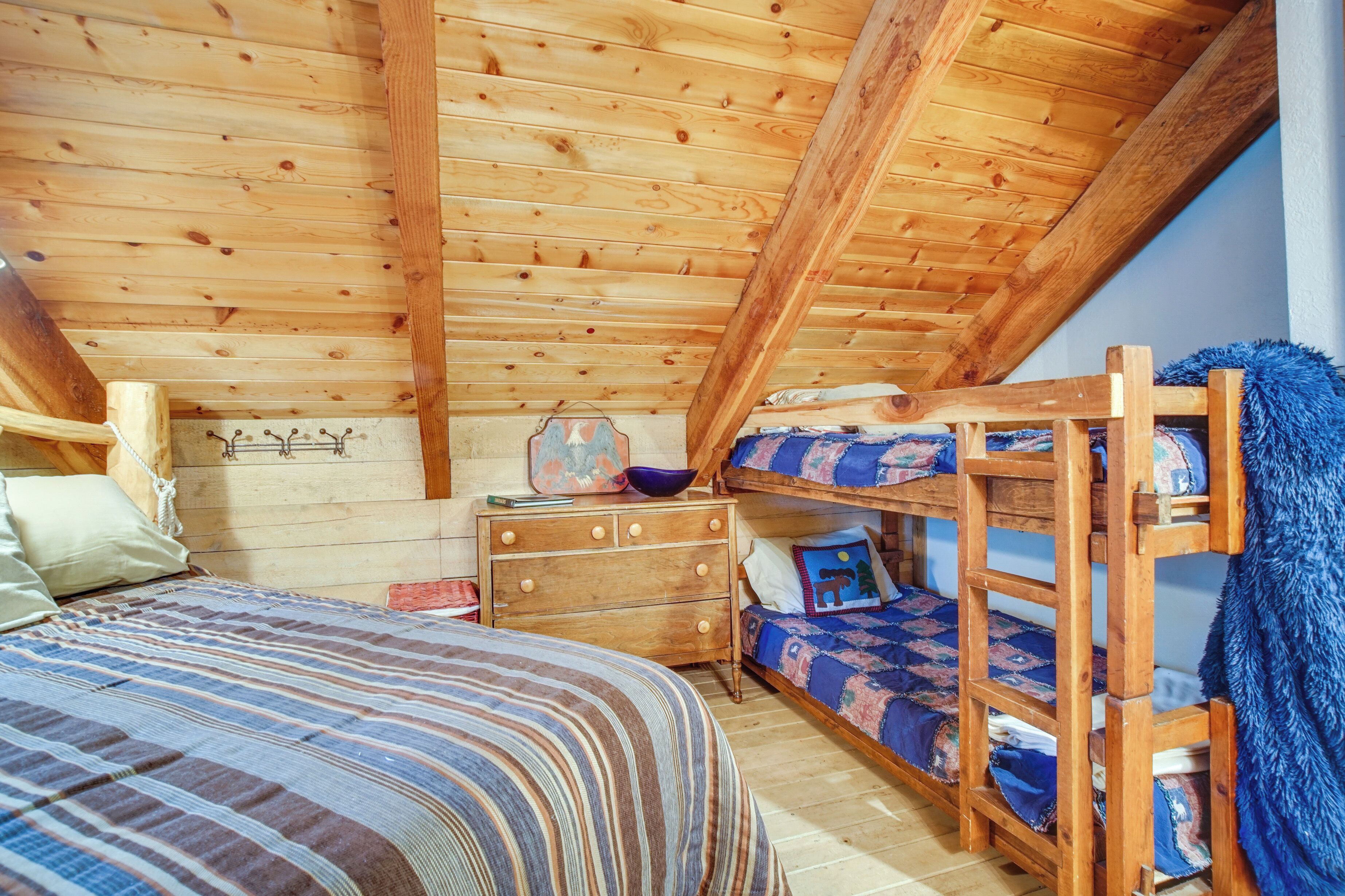 A wooden bunk bed with a blue blanket, a wooden dresser, and a striped bedspread in a room with wooden walls and ceiling.