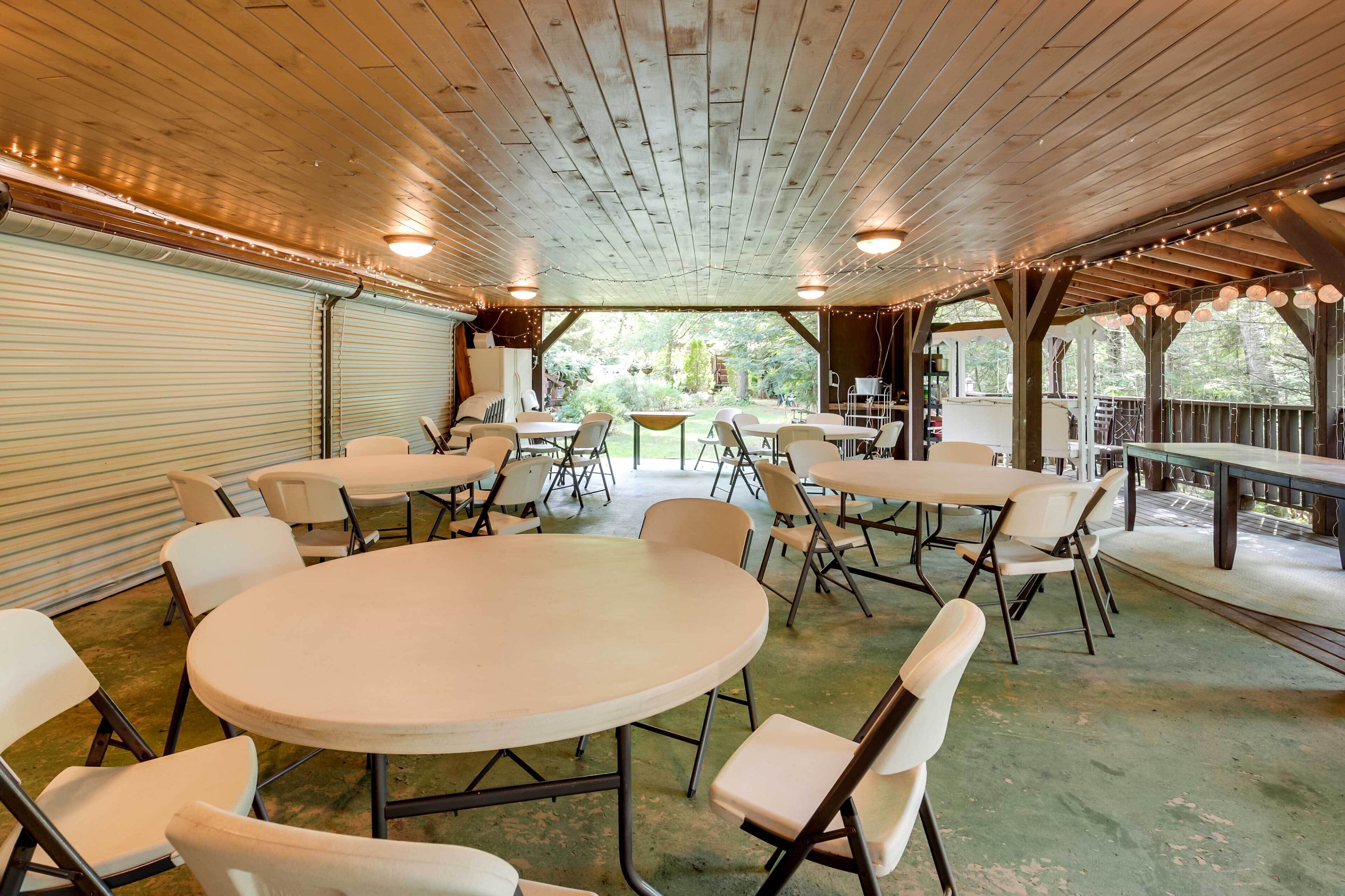 A covered outdoor dining area with tables and chairs, a view of the garden, and a wooden ceiling.
