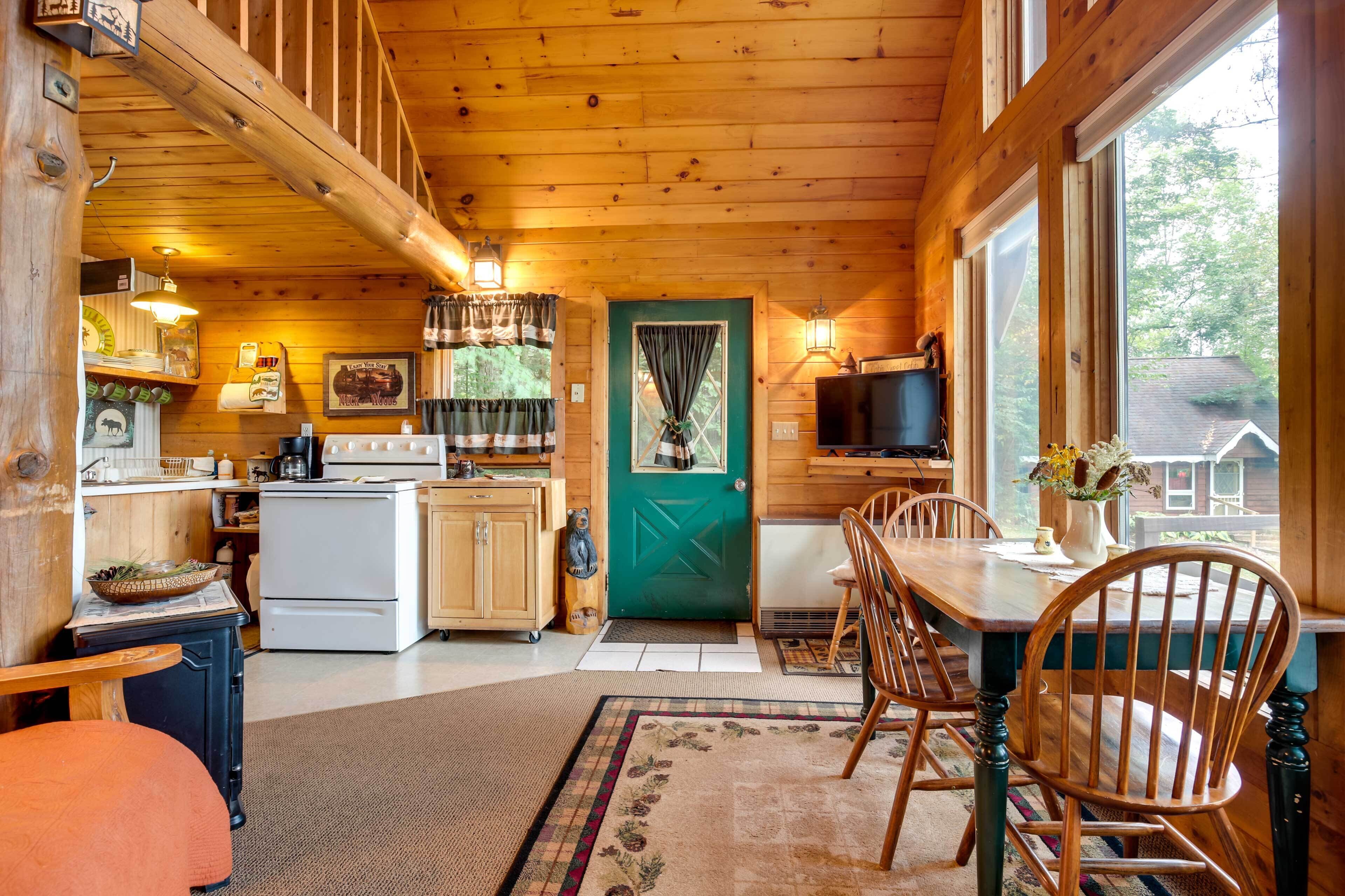 A wooden cabin interior with a kitchen, dining area, and a green door.