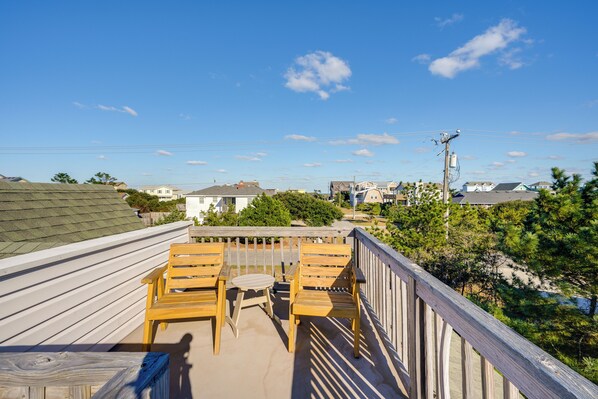 A wooden deck with two chairs and a table, overlooking a residential area with houses and trees.