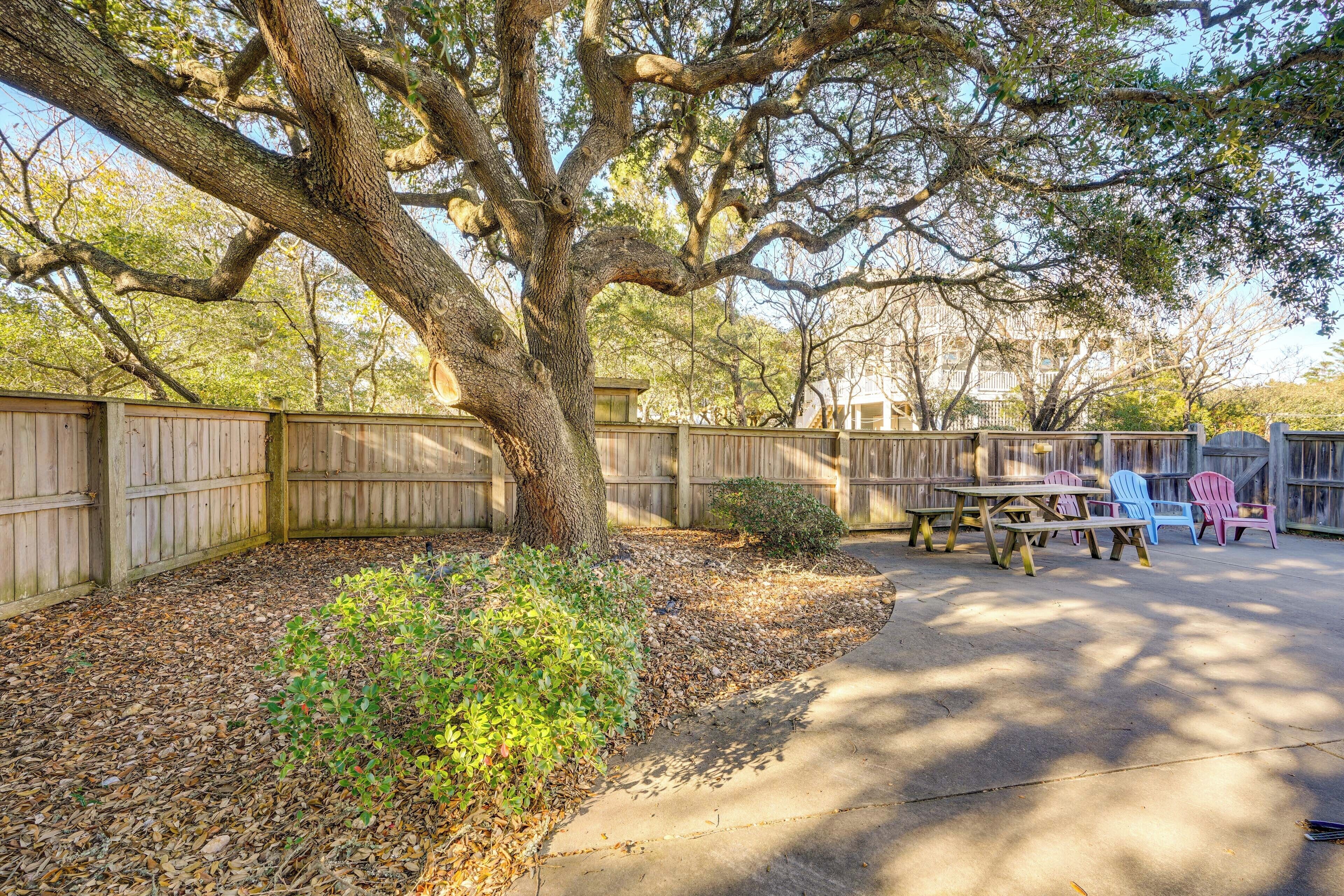 A backyard with a wooden fence, a picnic table, and colorful Adirondack chairs.