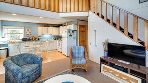 A spacious living area with a high ceiling, wooden staircase, and a modern kitchen in the background. - Kitty Hawk Vacation Rental w/ Private Pool! (Kitty Hawk)