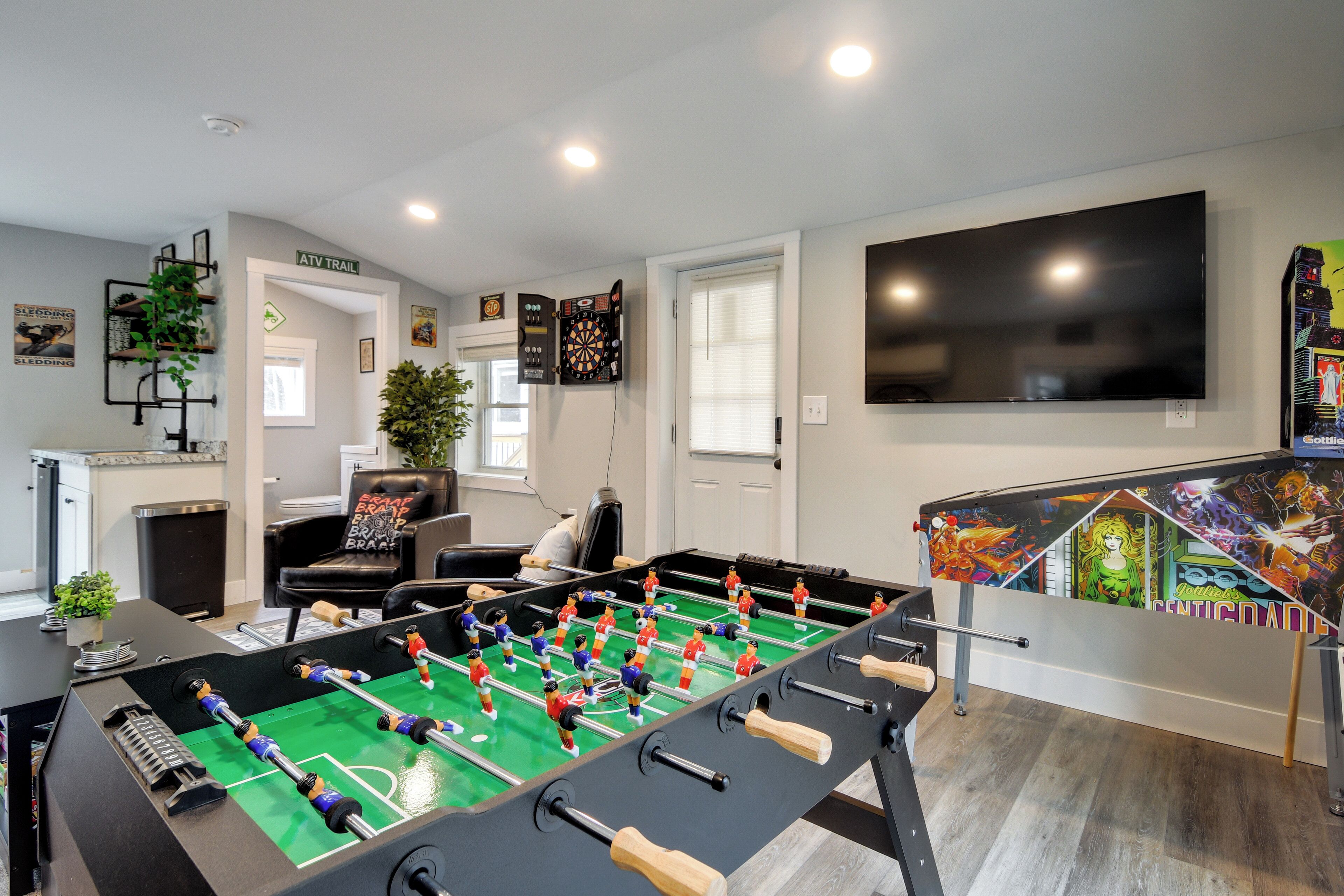 Una habitación con mesa de futbolín, dardos, televisor y mesa de futbolín con panel posterior de colores.